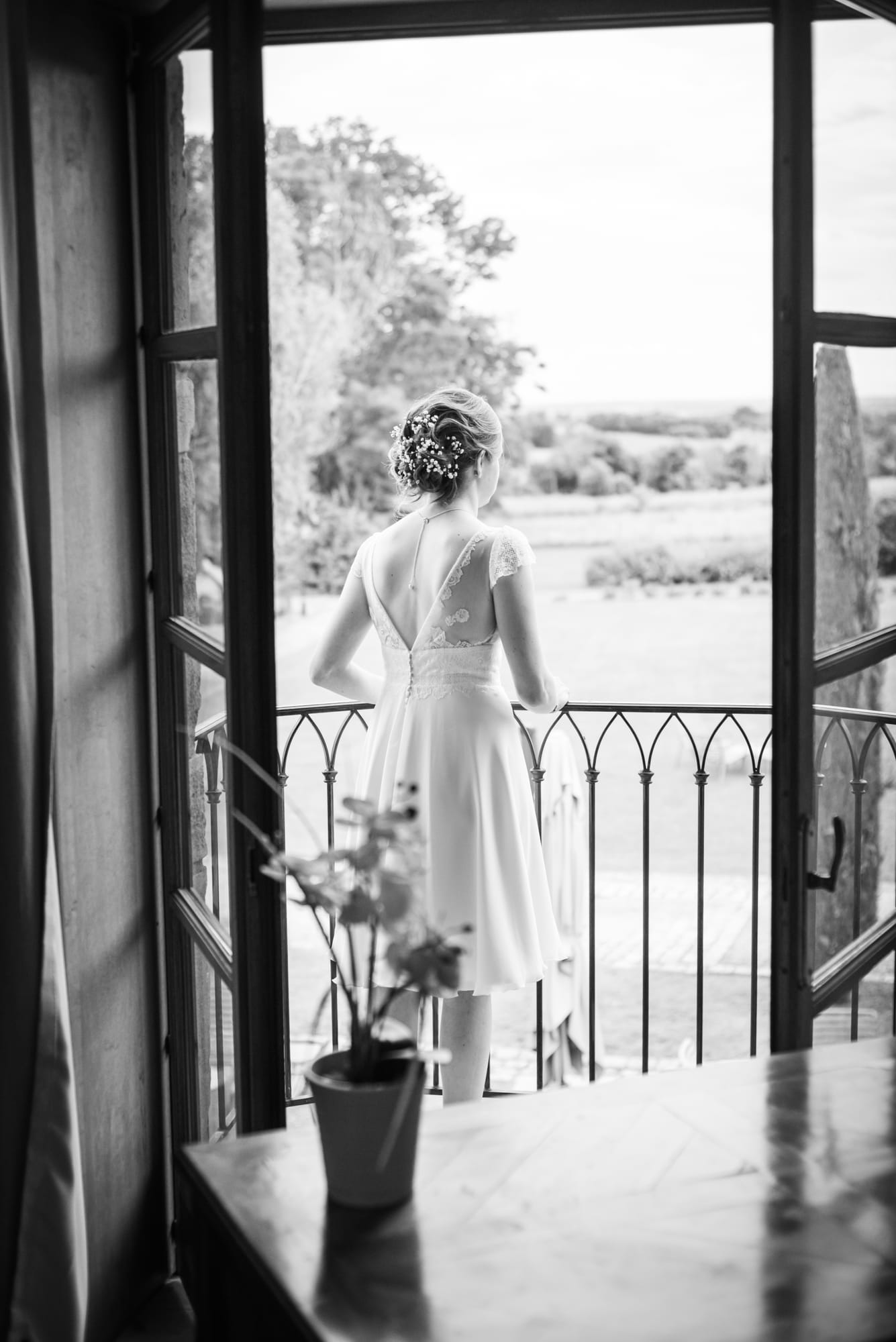 Mariée de dos sur un balcon, regardant les collines à travers les portes ouvertes