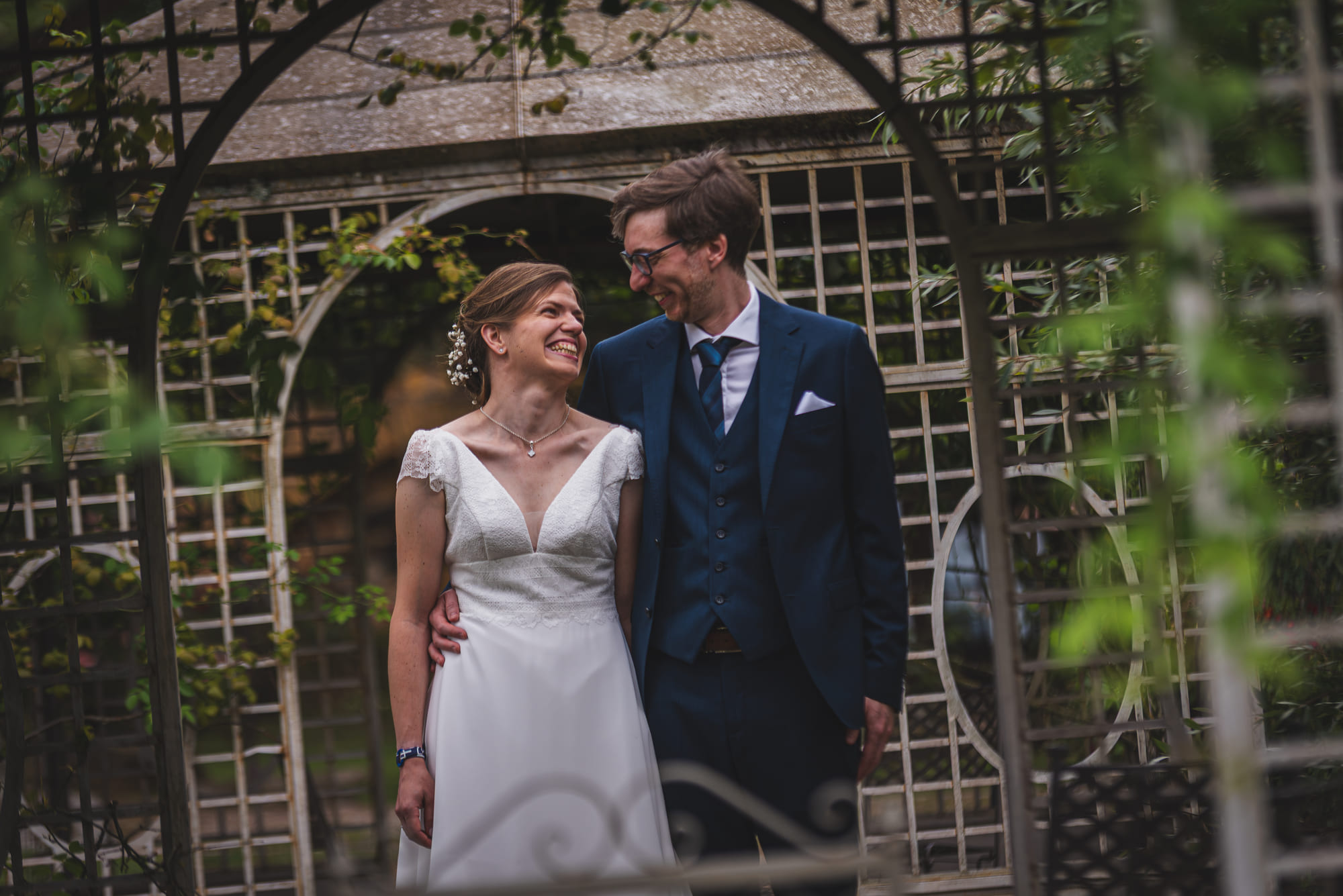 Laure et Mathieu souriants dans le jardin du Domaine de la Ruisselière, cadrés par une gloriette